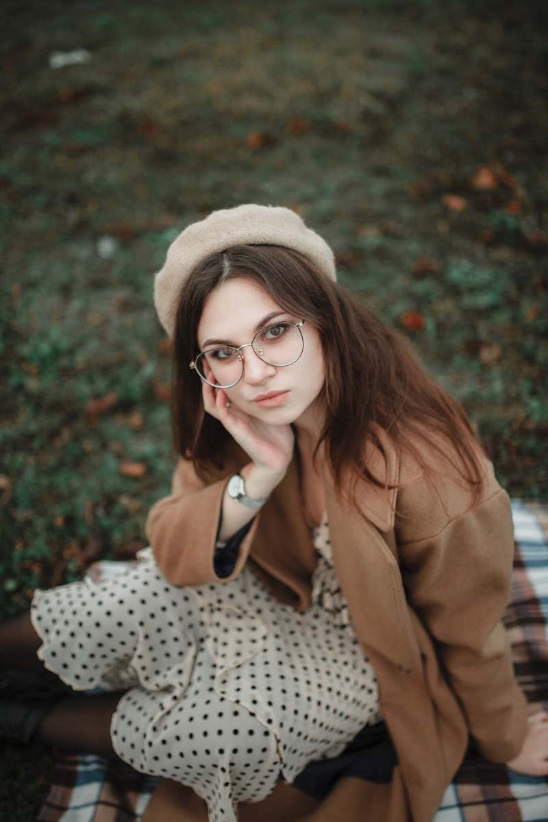 clothing woman wearing brown coat sitting on ground during daytime glasses