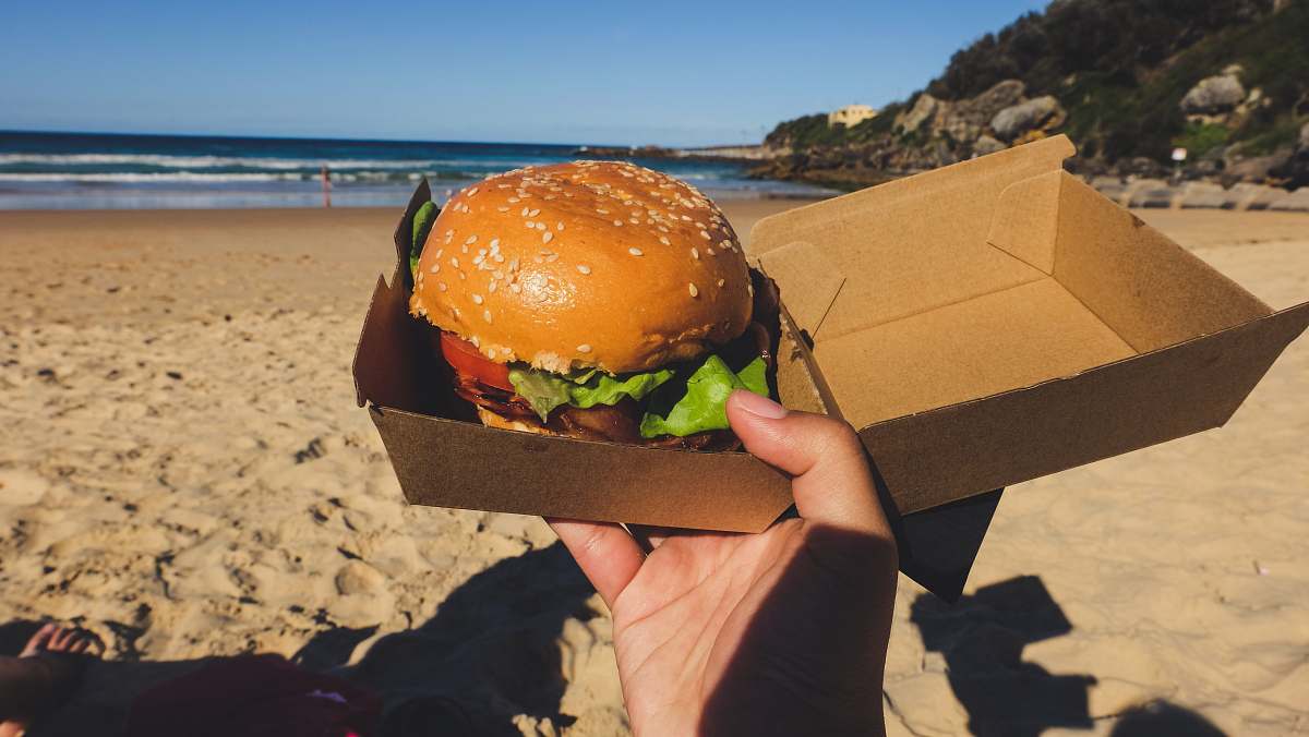 food person holding box with burger and lettuce sandwich