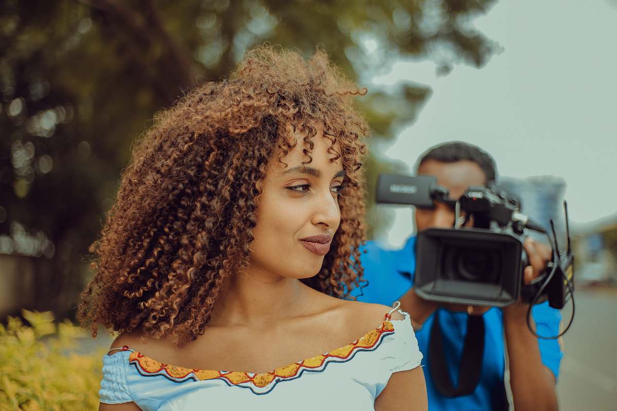 human woman smiling and looking at her right in front of man using video camera person