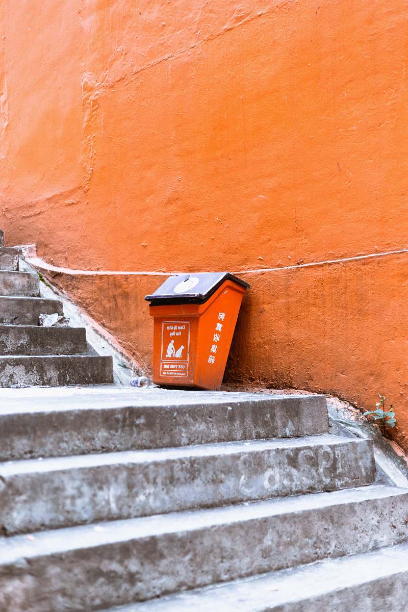 banister orange and black plastic trash bin beside orange painted wall staircase