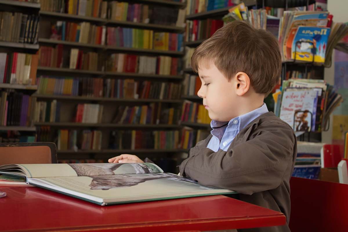person boy sitting near red table reading book people