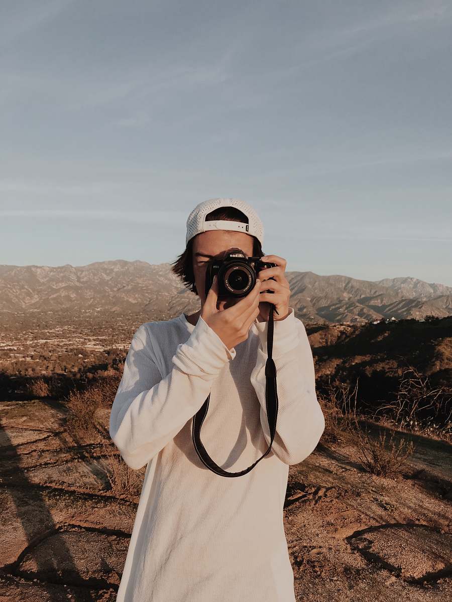 person man holding camera standing near mountain ranges photographer
