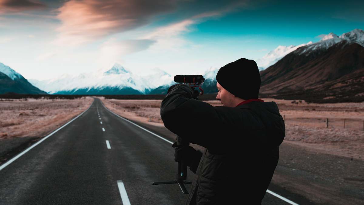person man holding camera while standing on paved road road