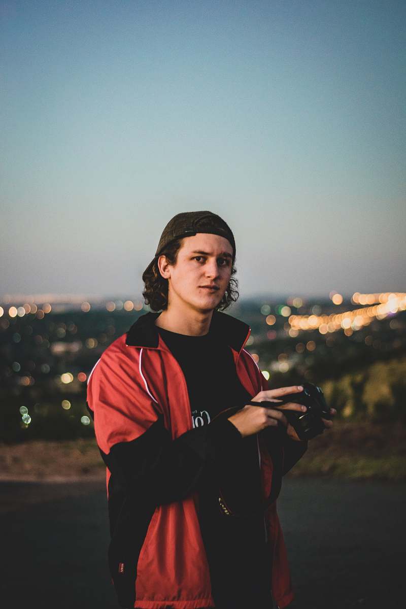 person man wearing red and black zip-up jacket standing outdoor during daytime photographer