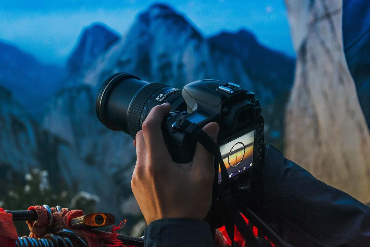 A man expertly holds a DSLR camera, capturing the breathtaking beauty of a majestic mountain landscape. This scene showcases the perfect blend of adventure and photography, ideal for travel blogs, outdoor lifestyle articles, and promotional material for photography workshops. The vivid colors and stunning topography make this image a must-have for anyone seeking to convey the thrill of nature and the art of capturing it through the lens.
