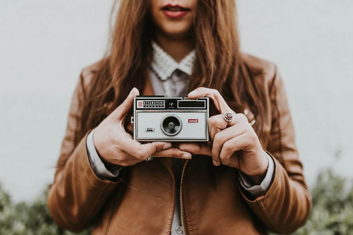 In this captivating image, a woman stands confidently holding a camera, ready to capture life's spontaneous moments. Her passionate expression reflects a love for photography, making it a perfect representation of creative artistry. This photo is ideal for blogs, marketing materials, or any content related to photography, travel, or women's empowerment in creative fields.