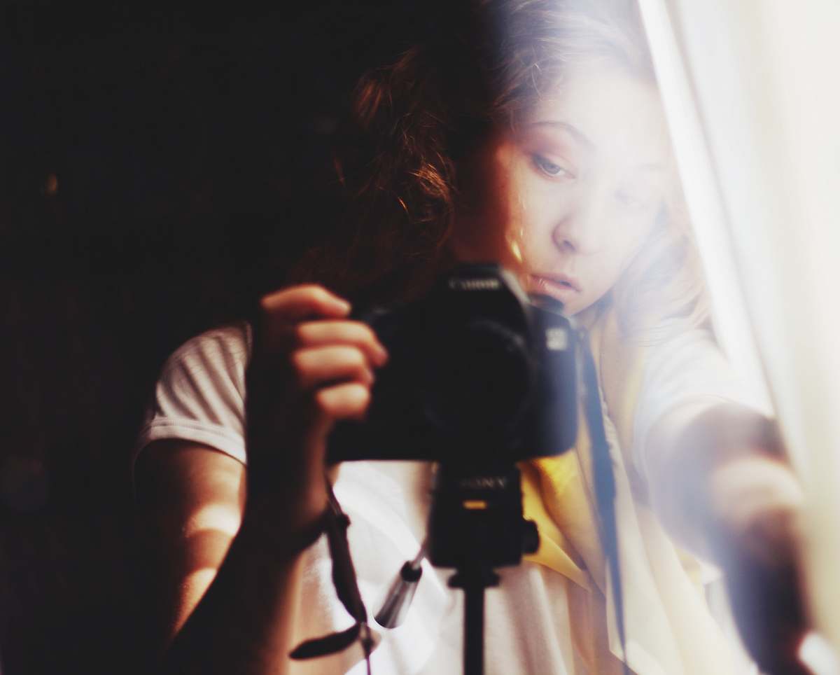 person woman holding DSLR camera beside white curtain photographer