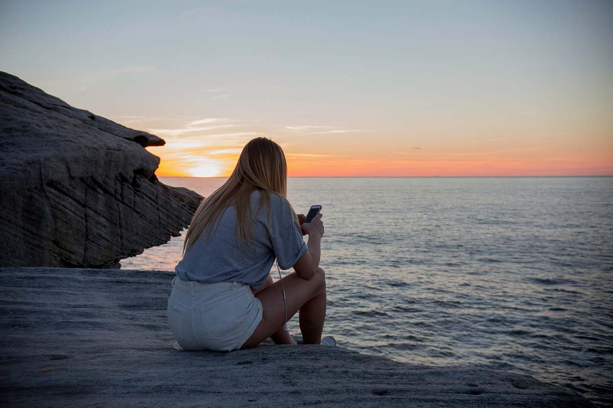 person woman in grey shirts and white sorts sits on rock cliff by the beach photo