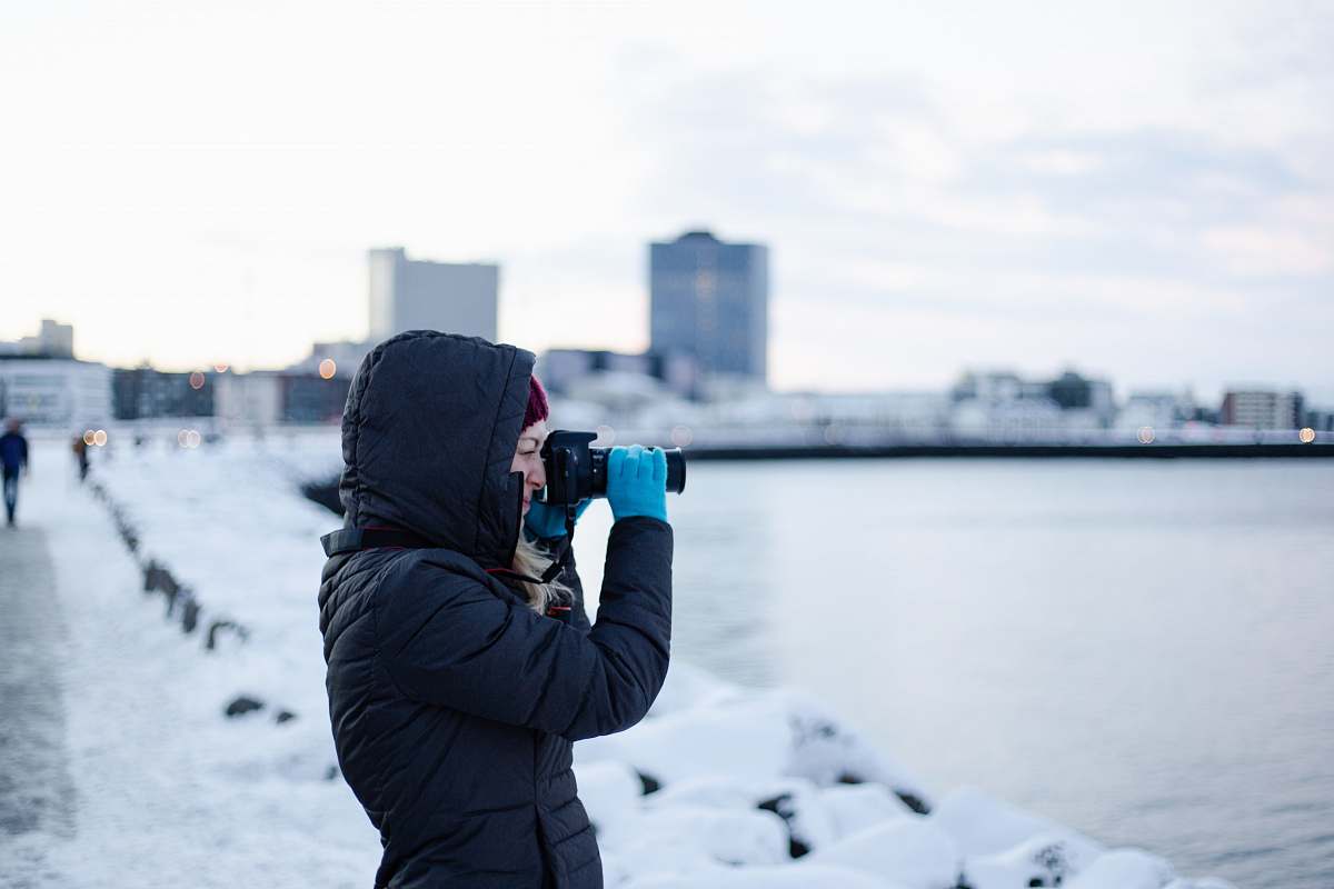 person woman wearing black hooded jacket using DSLR camera photographer