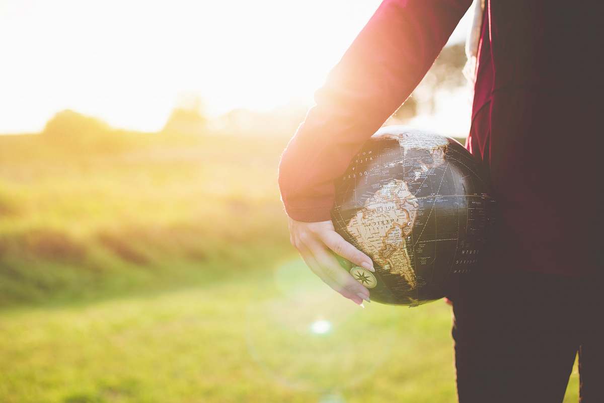 world person holding black and brown globe ball while standing on grass land golden hour photography hand