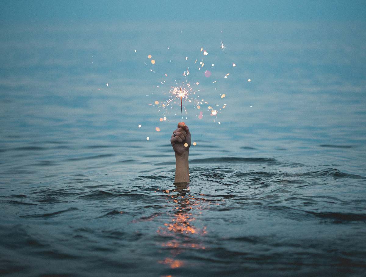 sparkle person submerged on body of water holding sparkler holding