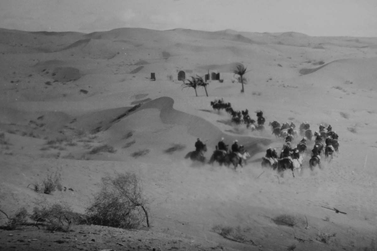 grey grayscale photo of men riding horses on desert outdoors