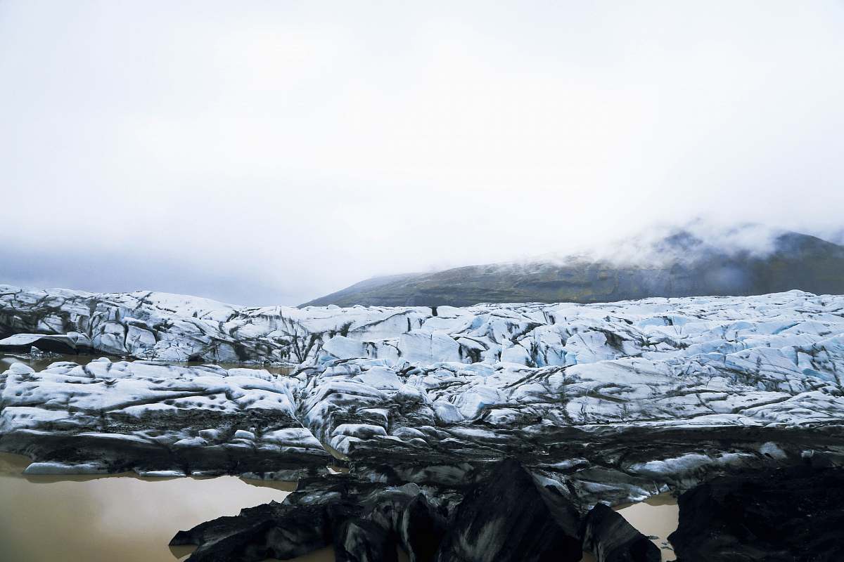 glacier snow covered rocky field near body of water during daytime snow