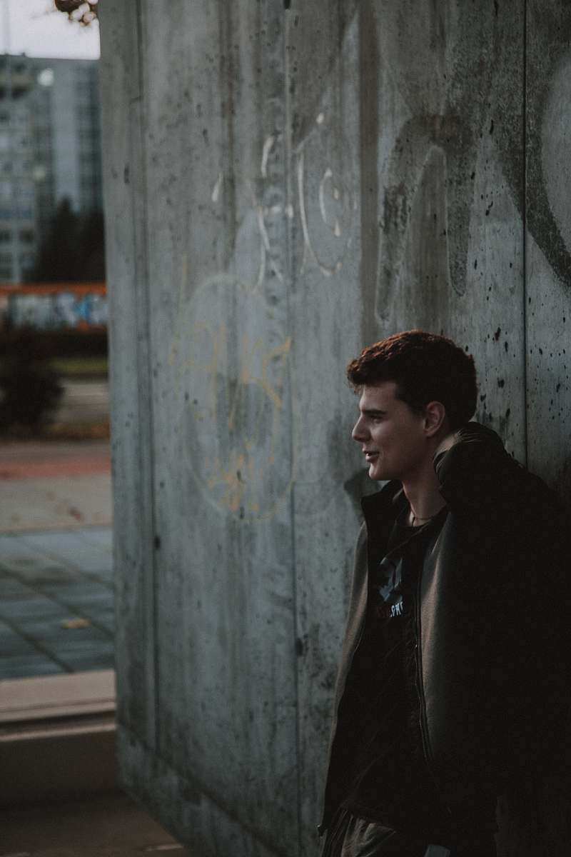 clothing man wearing jacket leaning on wooden wall during daytime man