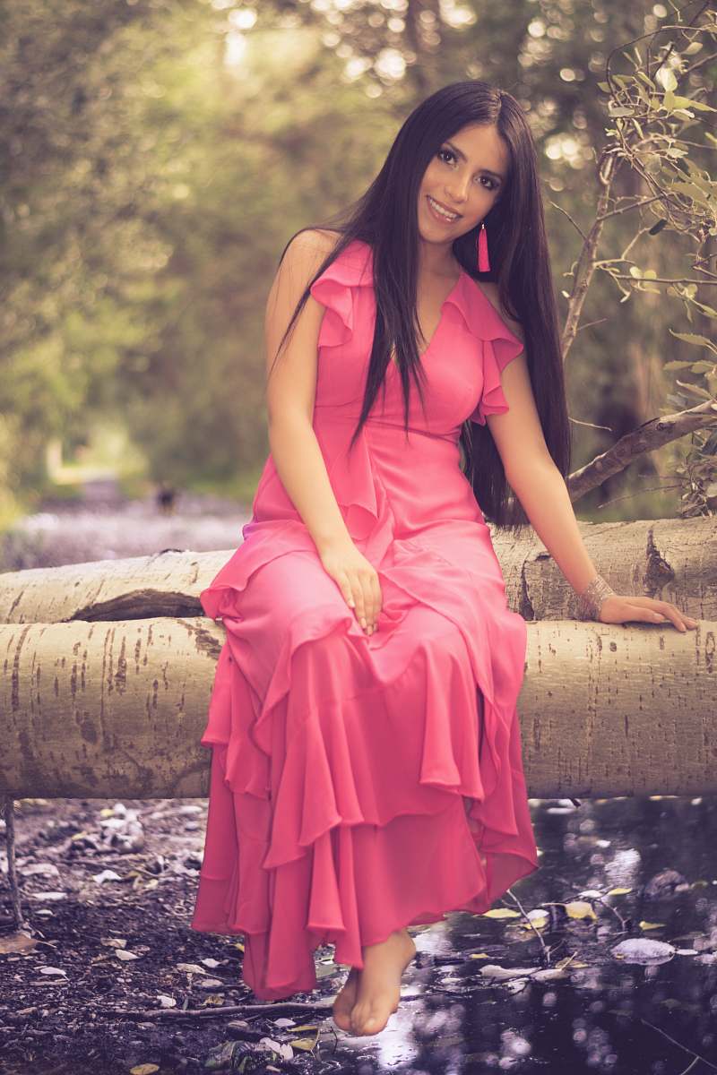 clothing smiling woman wearing pink halter dress sitting on tree trunk during daytime evening dress