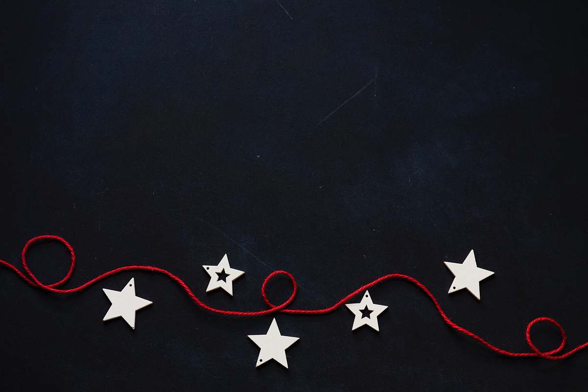 holiday white stars cutout on black surface with red string blackboard