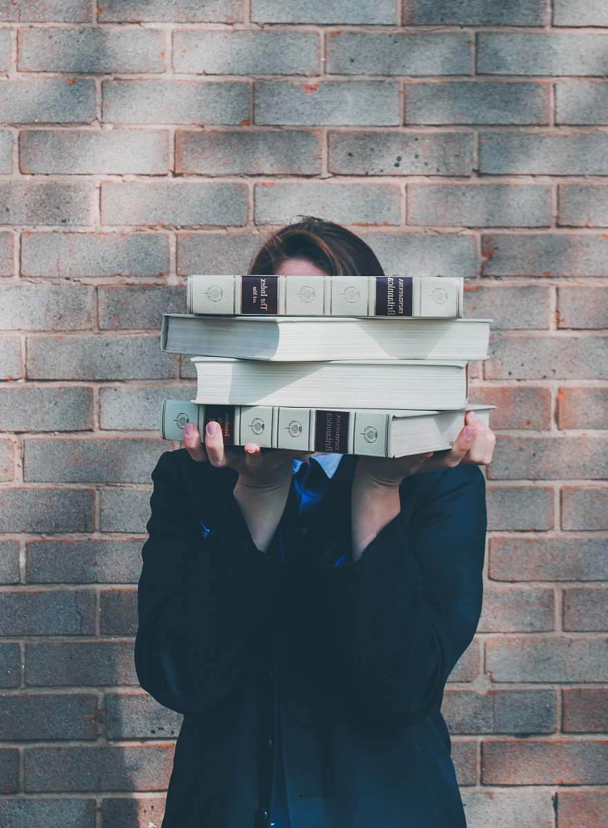apparel person holding pile of books near face grey