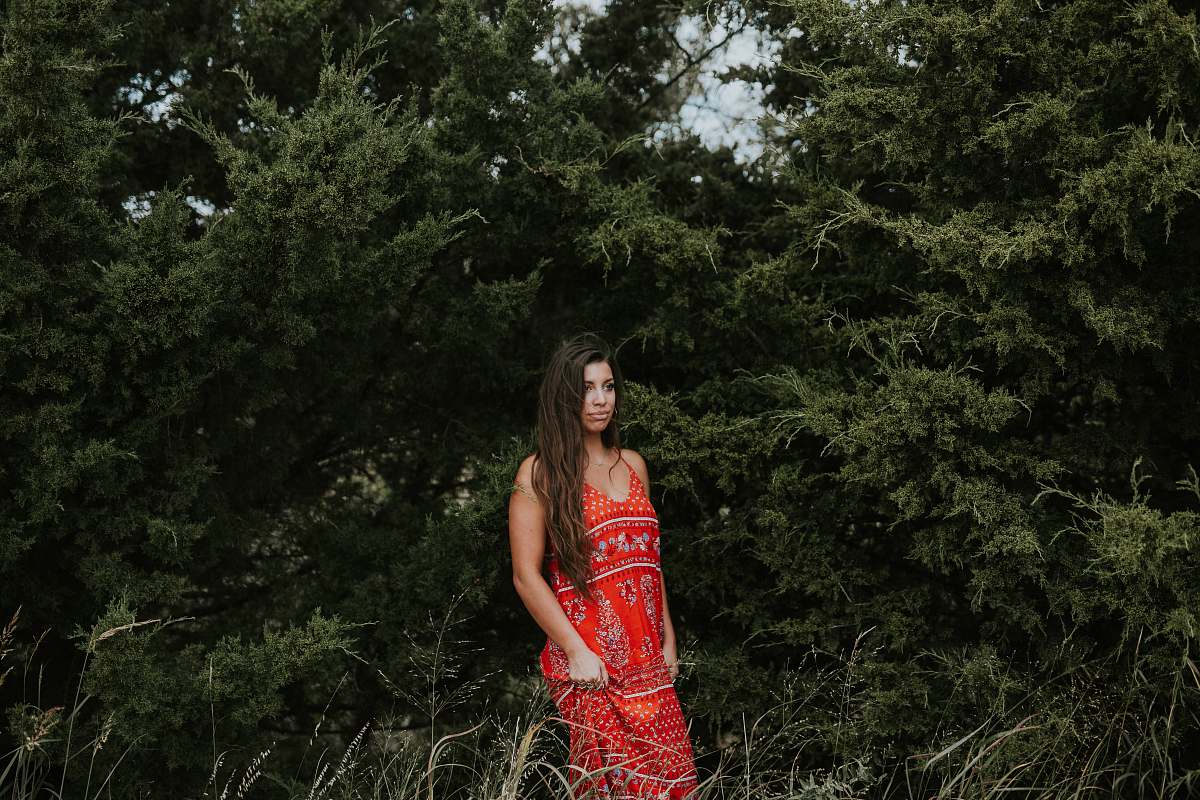 apparel woman in red spaghetti-strap dress standing beside green trees evening dress