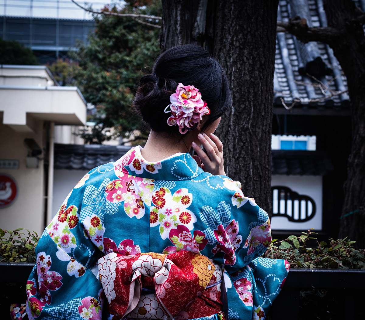 fashion woman wearing blue and multicolored floral kimuno standing and facing near tree apparel