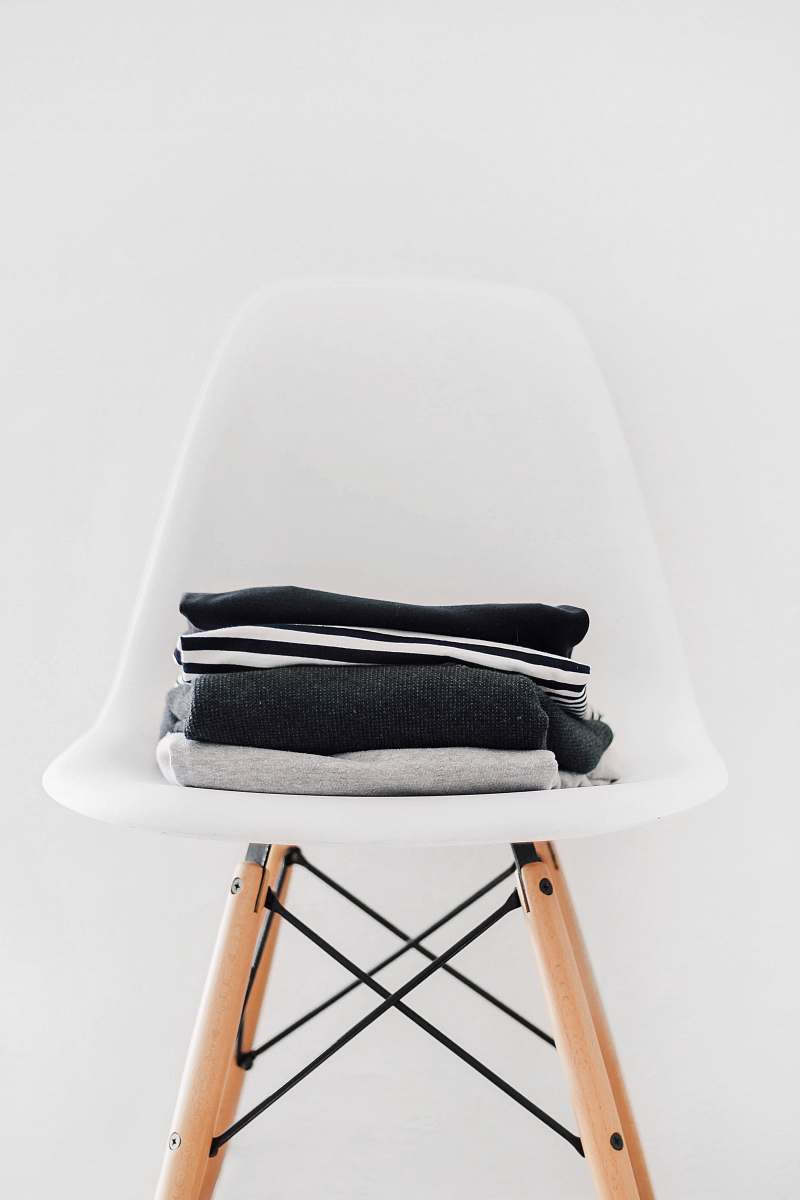 interior pile of black, white, and gray textiles on white padded chair with brown frame furniture