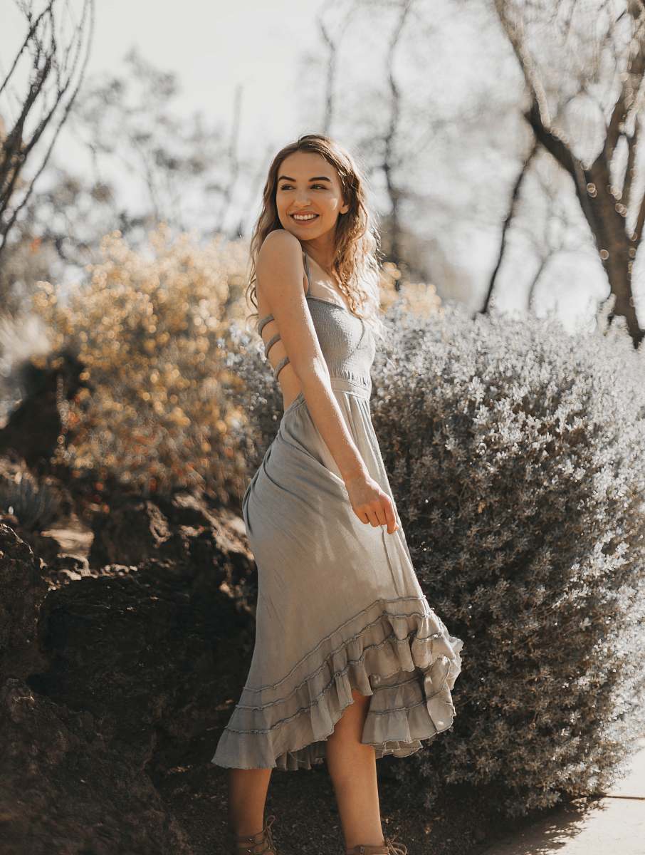 clothing woman in gray spaghetti strap dress standing near flower and smiling apparel