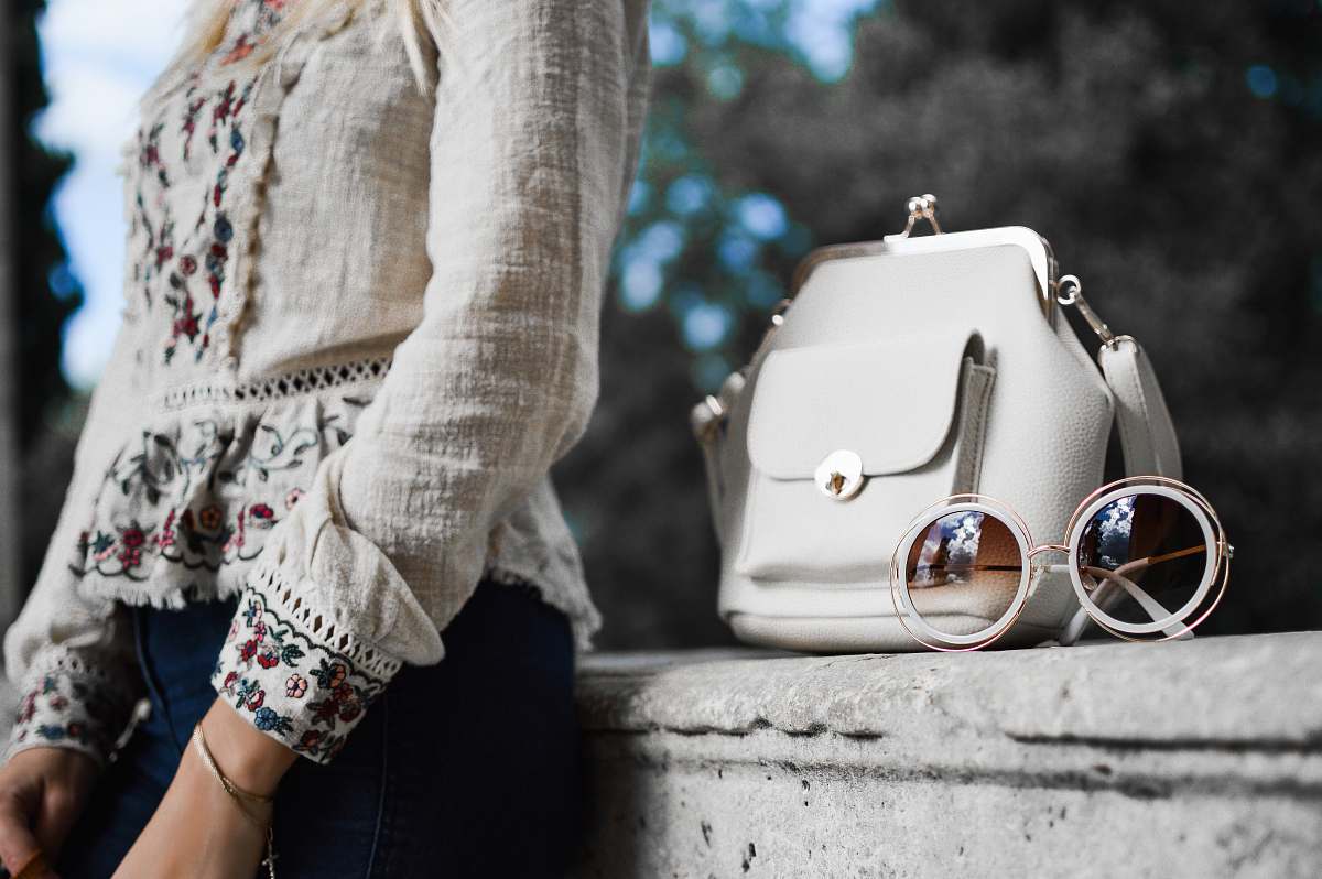 human woman wearing beige and red floral top leaning on gray concrete slab with white leather bag ontop person