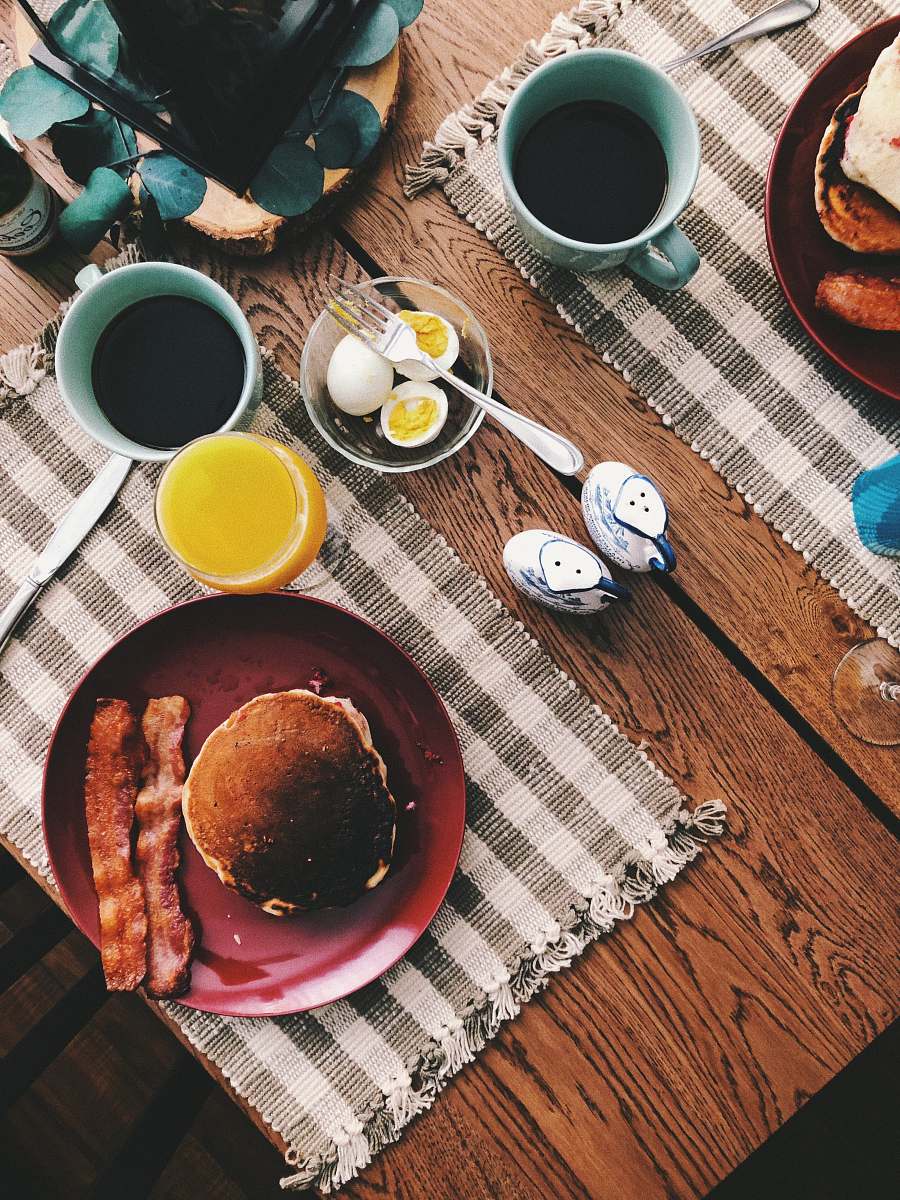 breakfast baked bread on round red ceramic plate near glass of orange juice, cup of coffee, and boiled eggs meal