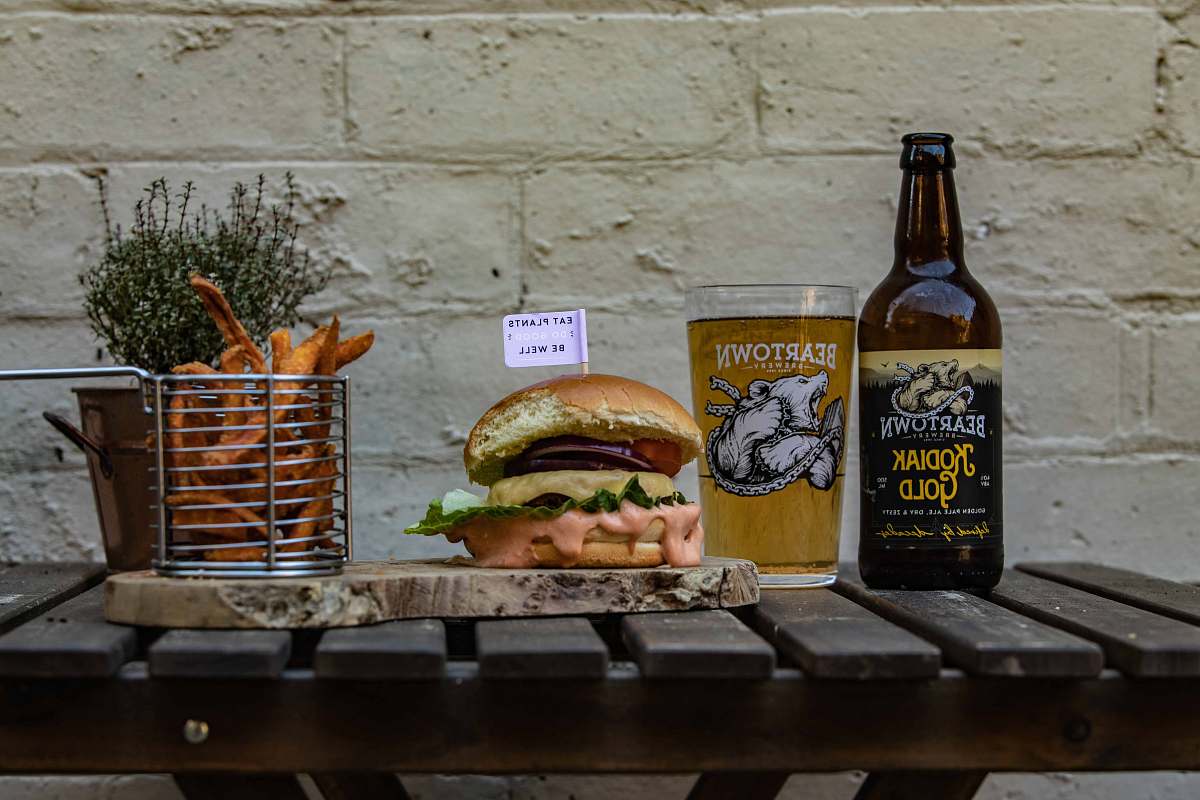 burger hamburger on chopping board by basket of fries and beer bottle alcohol