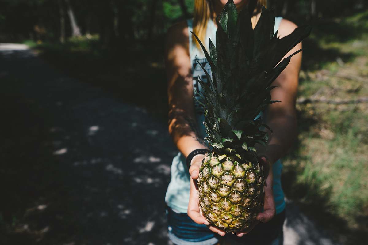 fruit person standing on gray pavement carrying pineapple fruit pineapple