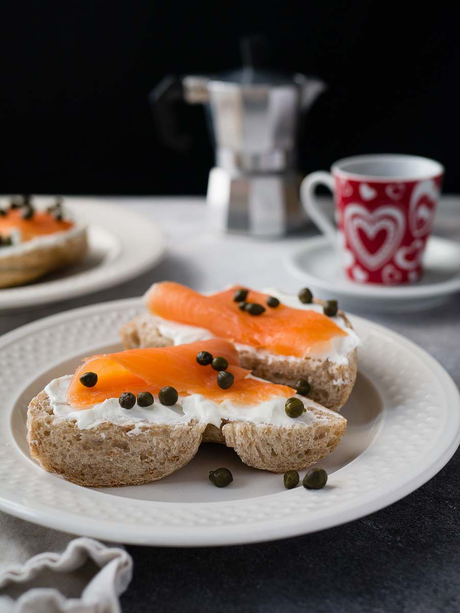 bagel tuna on bread with whip cream and pepper on round plate on top of table cup
