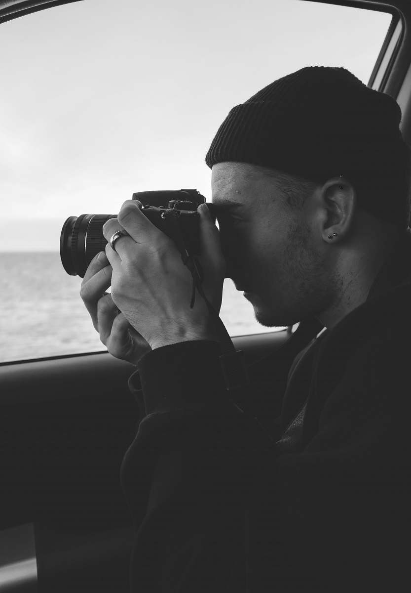 person grayscale photography of man holding DSLR camera black-and-white