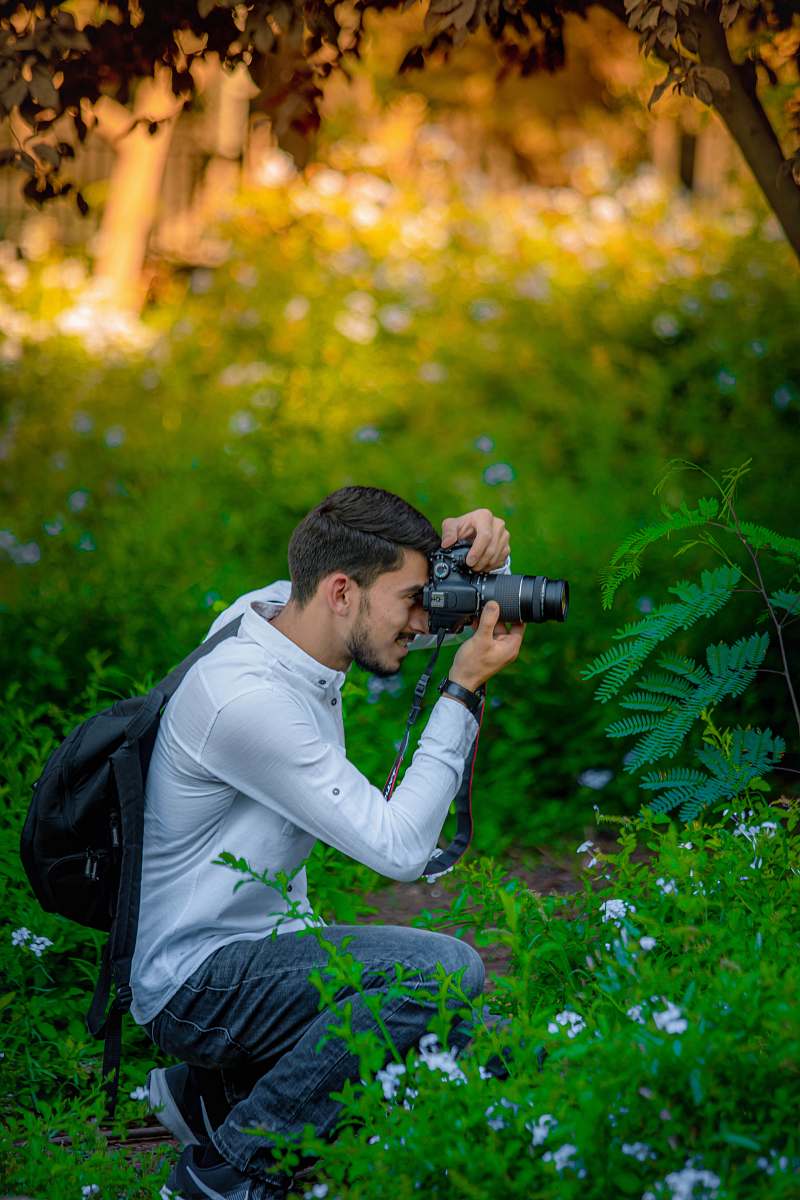 person man with black backpack sitting and taking photo on trees photo