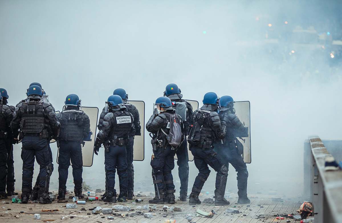 person riot police holding shield in front of smoke apparel