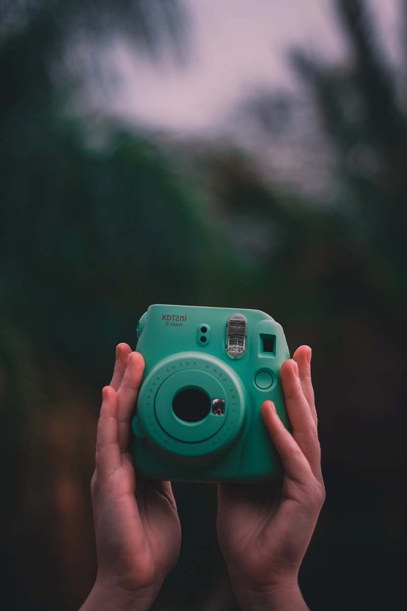 electronics selective focus photo of person holding teal Fujifilm Instax instant camera camera