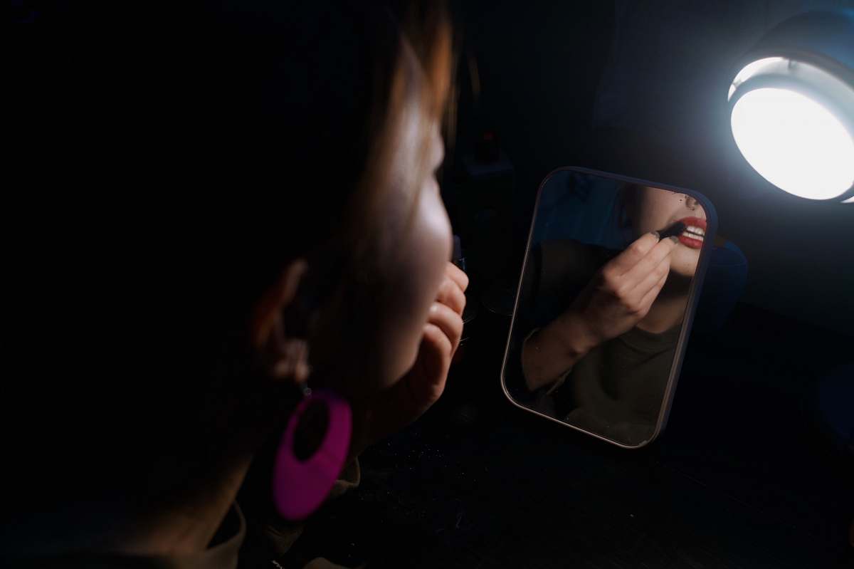 person woman facing the mirror putting lipstick on the lips hand