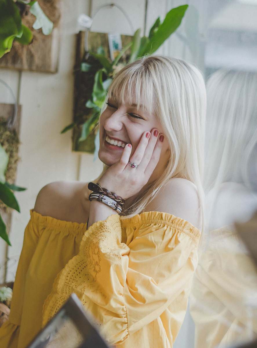 person smiling woman in yellow off-shoulder top holding her cheek human