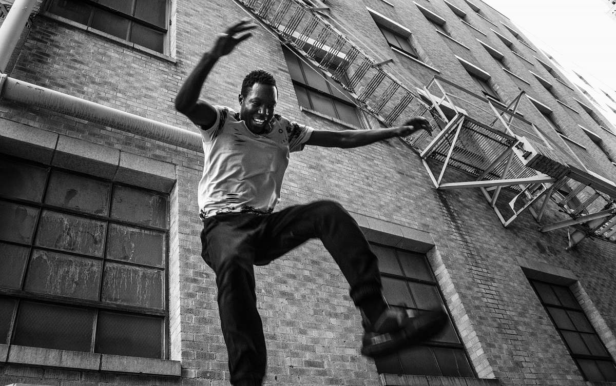 human grayscale photography of man jumping near building black-and-white