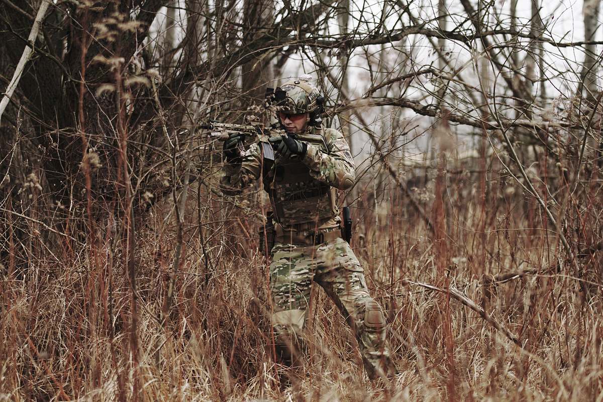 military man holding assault riffle beside bare tree military uniform