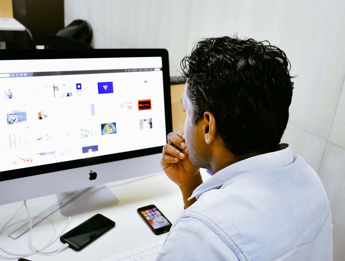 computer man sitting in front of silver Apple iMac on table human