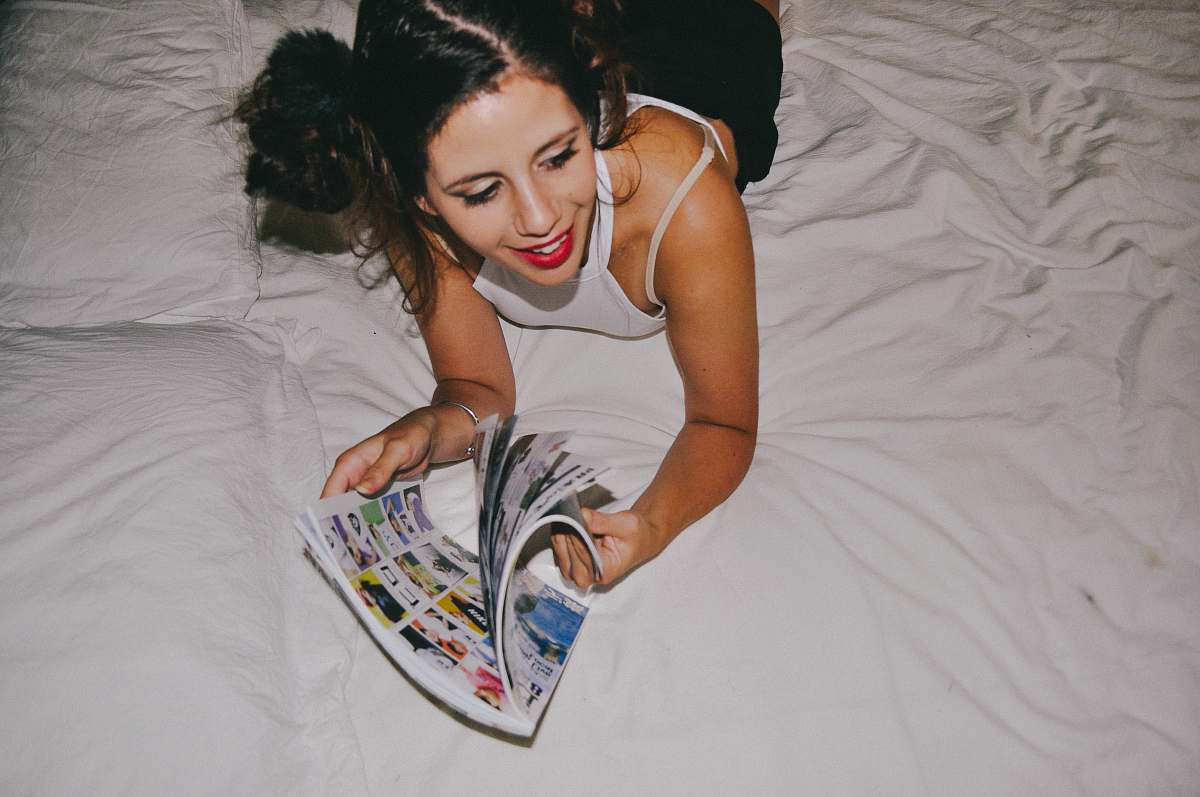 human smiling woman lying on bed while reading magazine bed