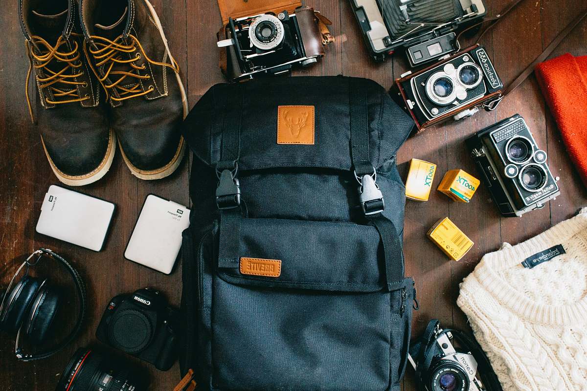 electronics high-angle photo of black bag beside cameras, portable HDD and black leather lace-up boots flatlay