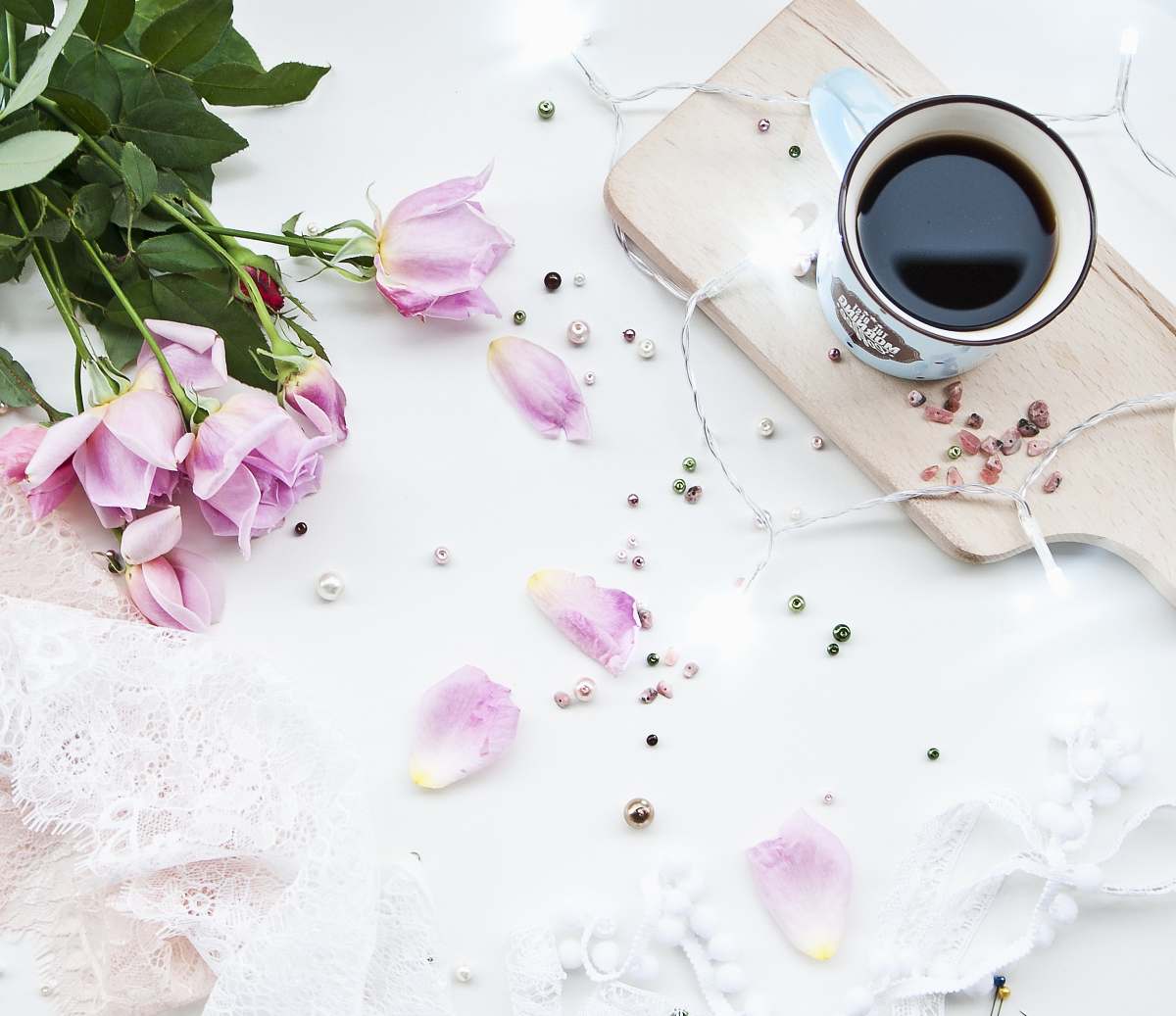 flower white ceramic mug filled with black liquid on beige chopping board beside pink roses on white surface rose