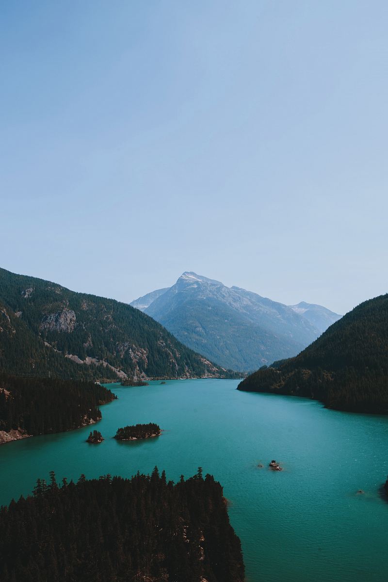 body of water between green and brown mountain range under clear blue sky during daytime