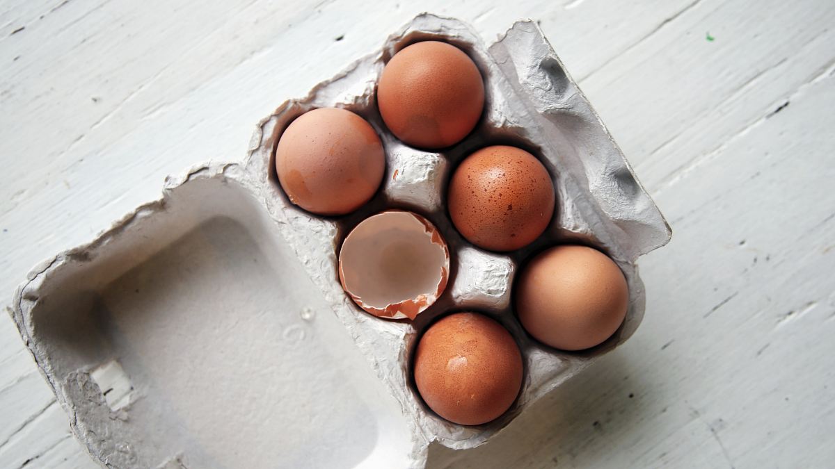 five whole eggs and one empty half-open egg inside open egg tray