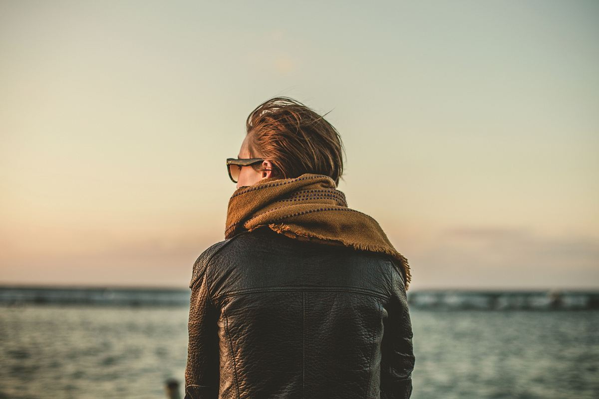 focus photo of person wearing black leather jacket with brown scarf near sea during daytime