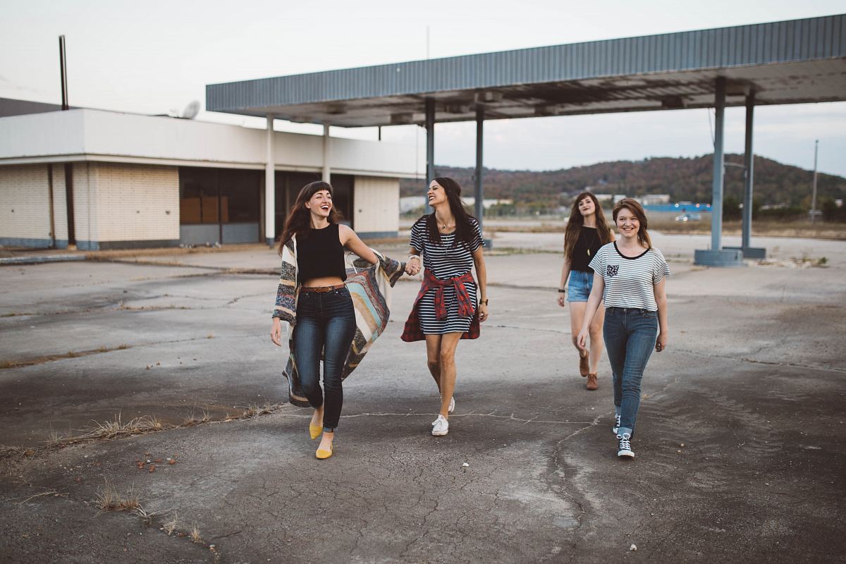four girls walking near warehouse during daytime