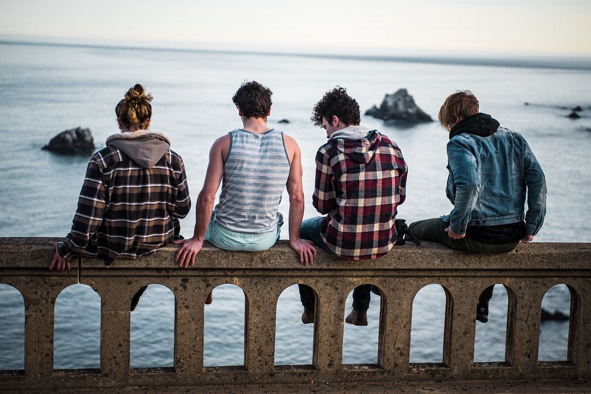 four person sitting on bench in front of body of water