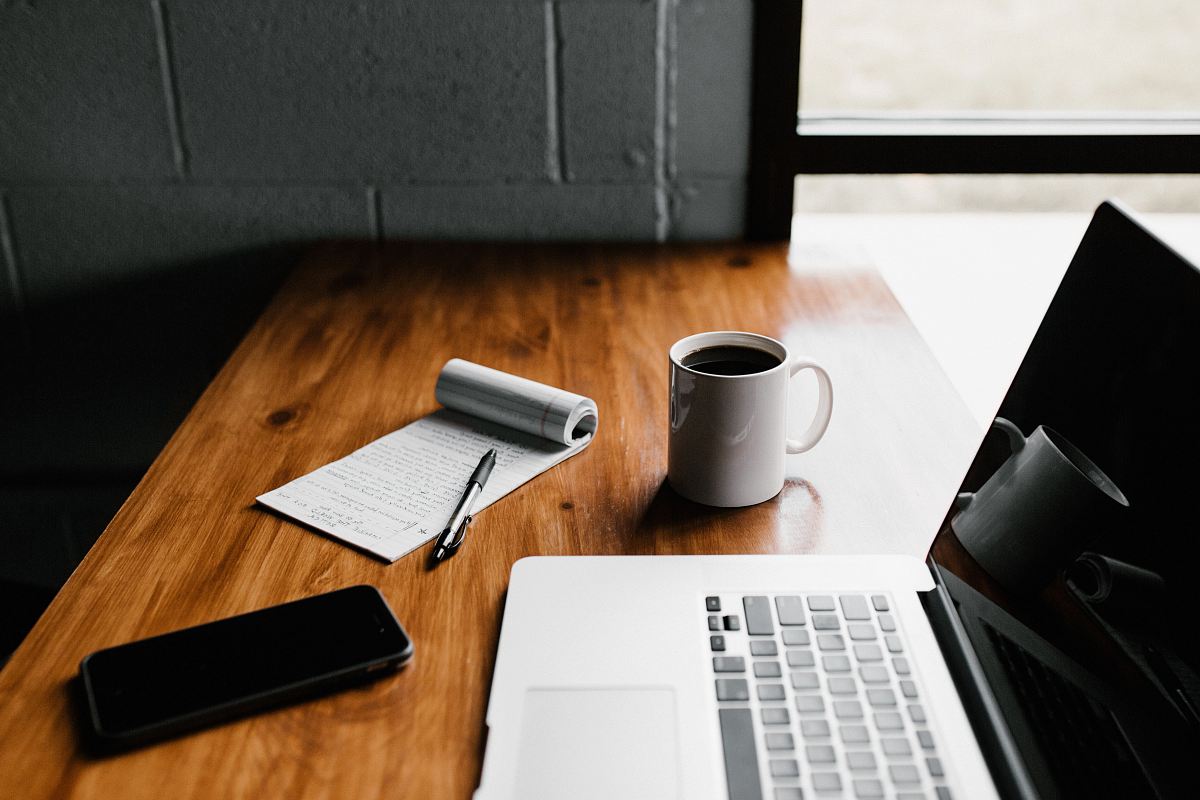 MacBook Pro, white ceramic mug,and black smartphone on table