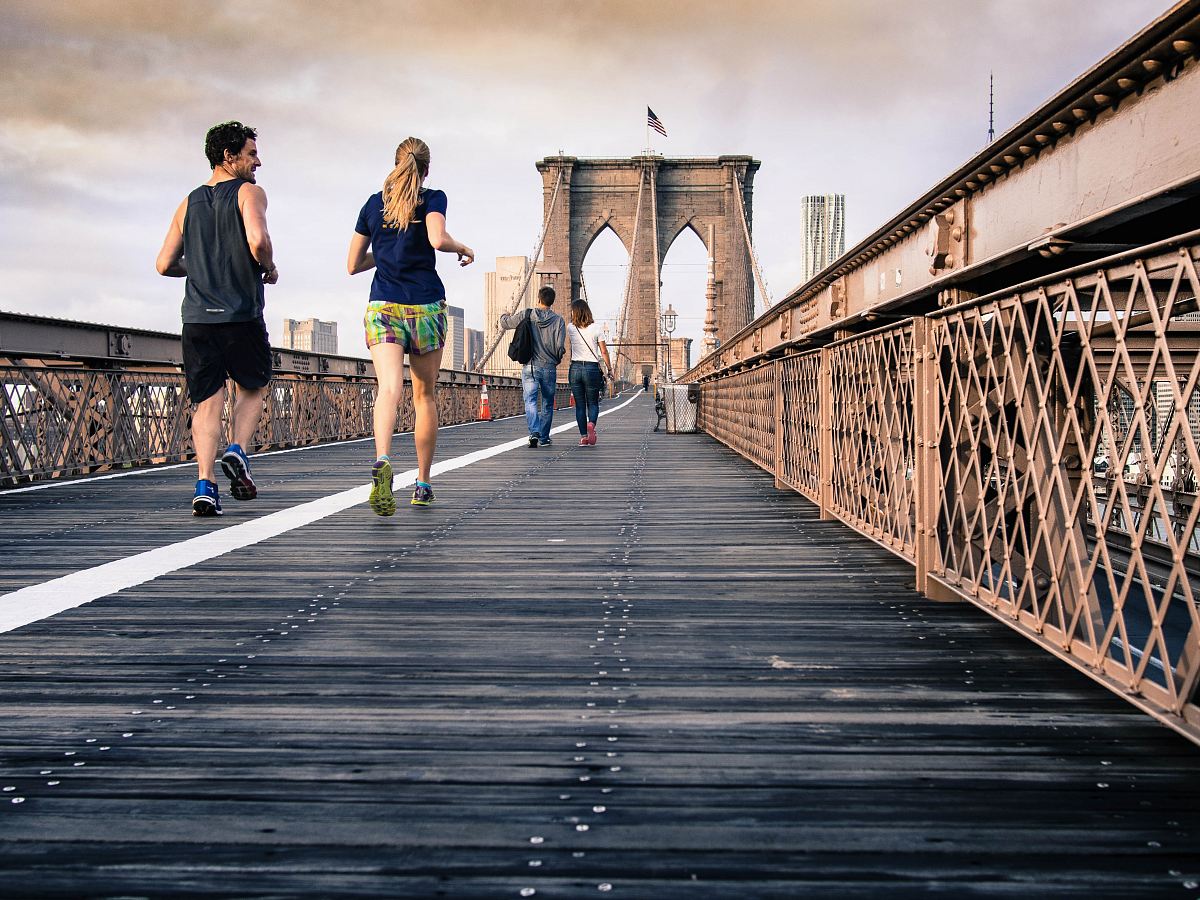 man and woman in black tops jogging at bridge under clear skies