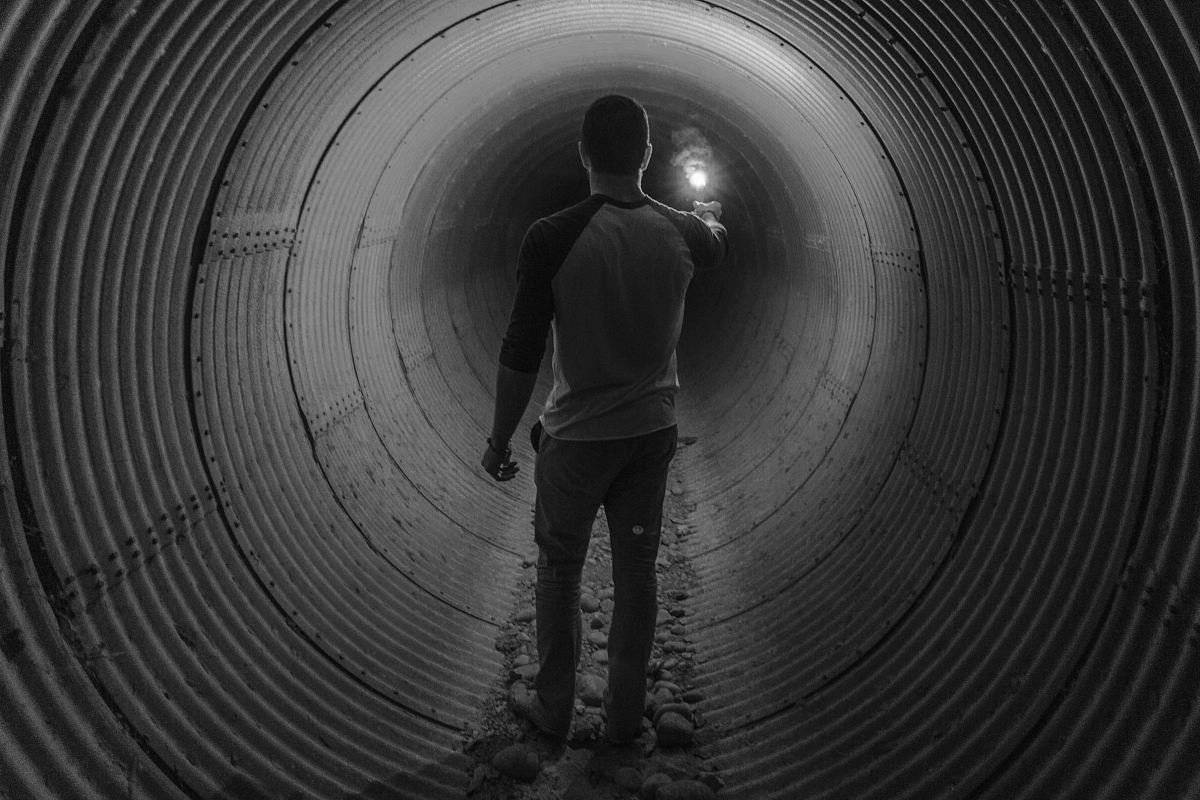 man holding light walking inside tunnel